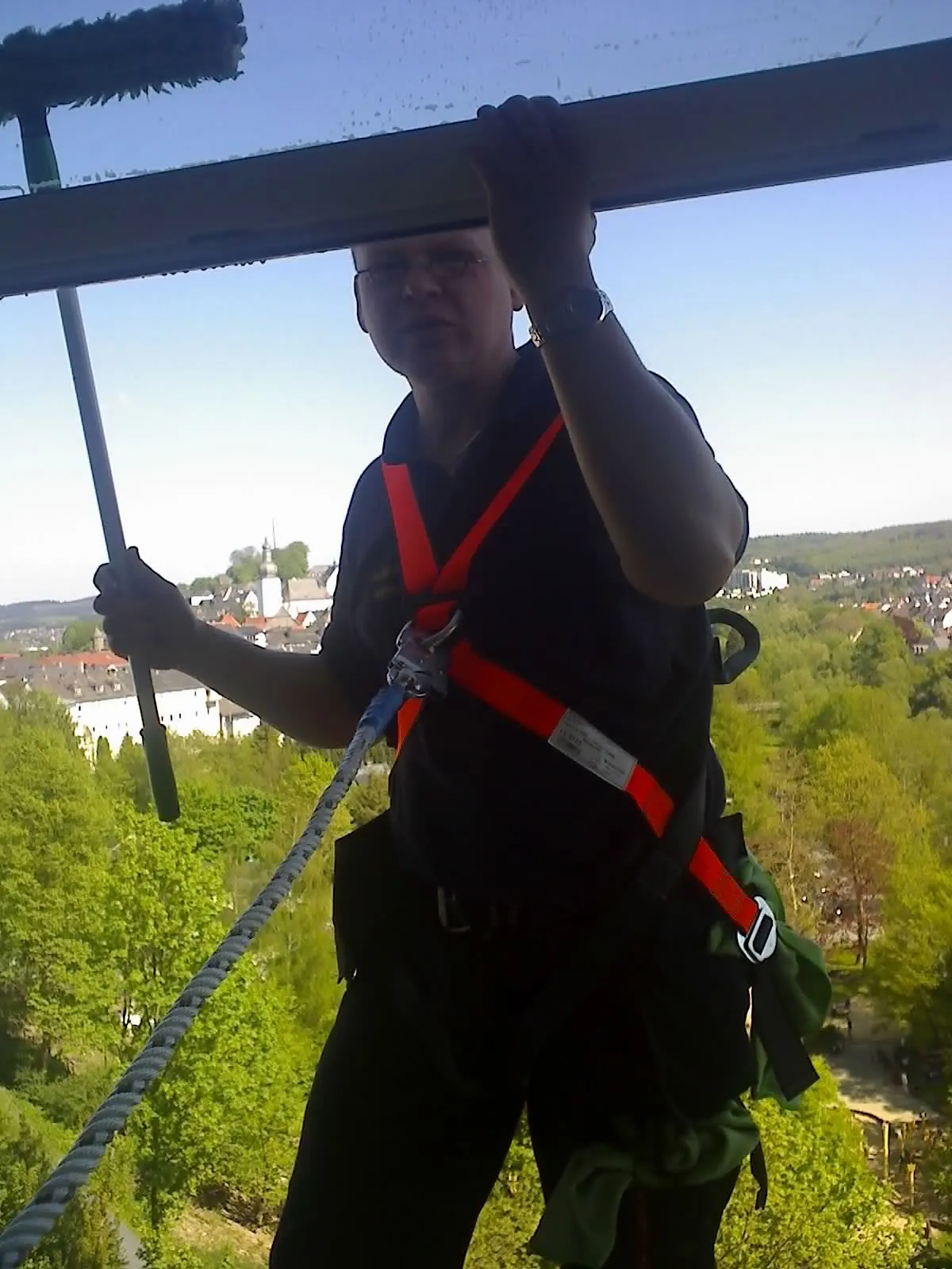 Mitarbeiter mit Absturzsicherung reinigt ein Glasdach von oben